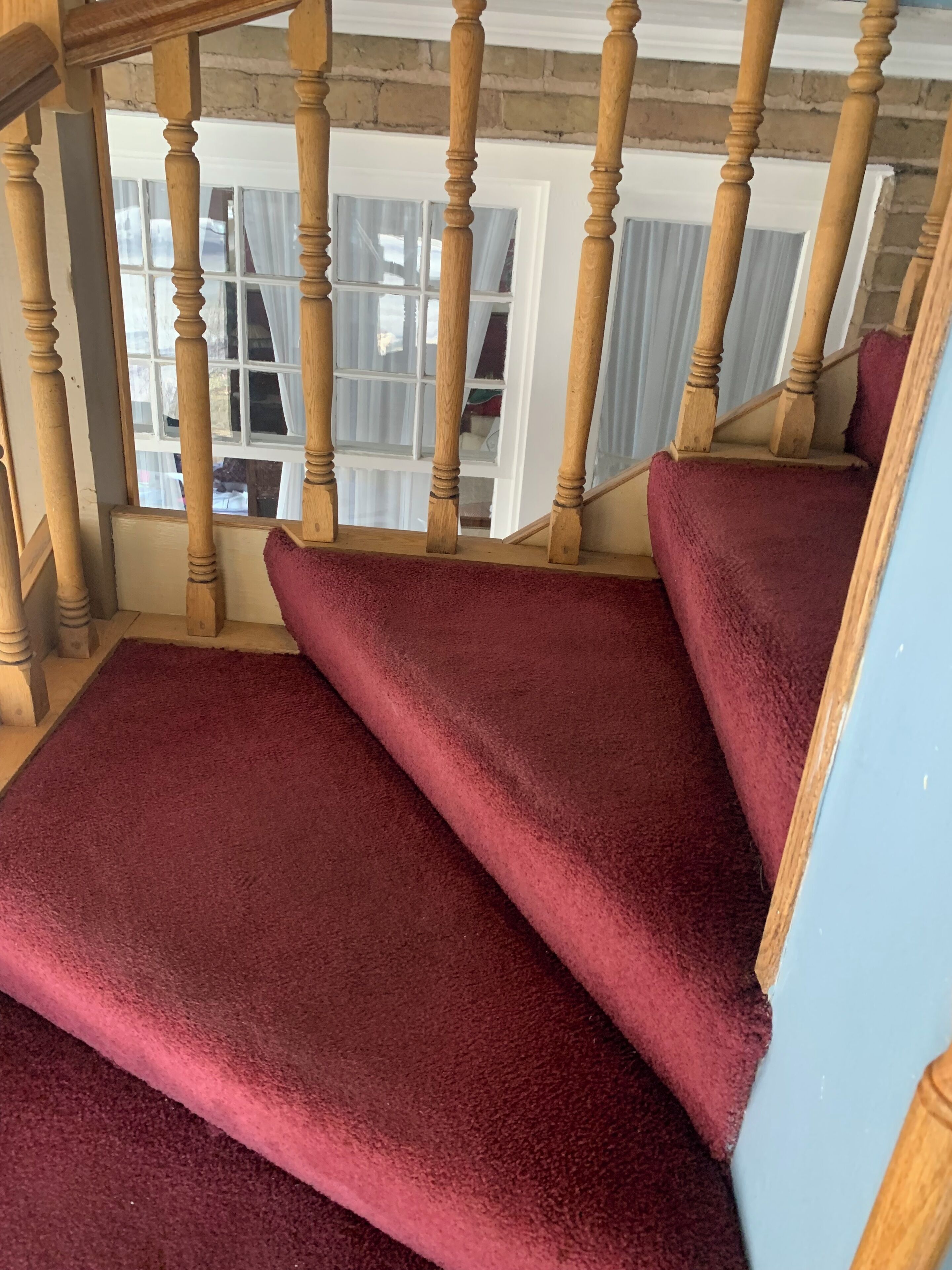 Un escalier avec des balustrades en bois et des marches recouvertes d’une moquette rouge.