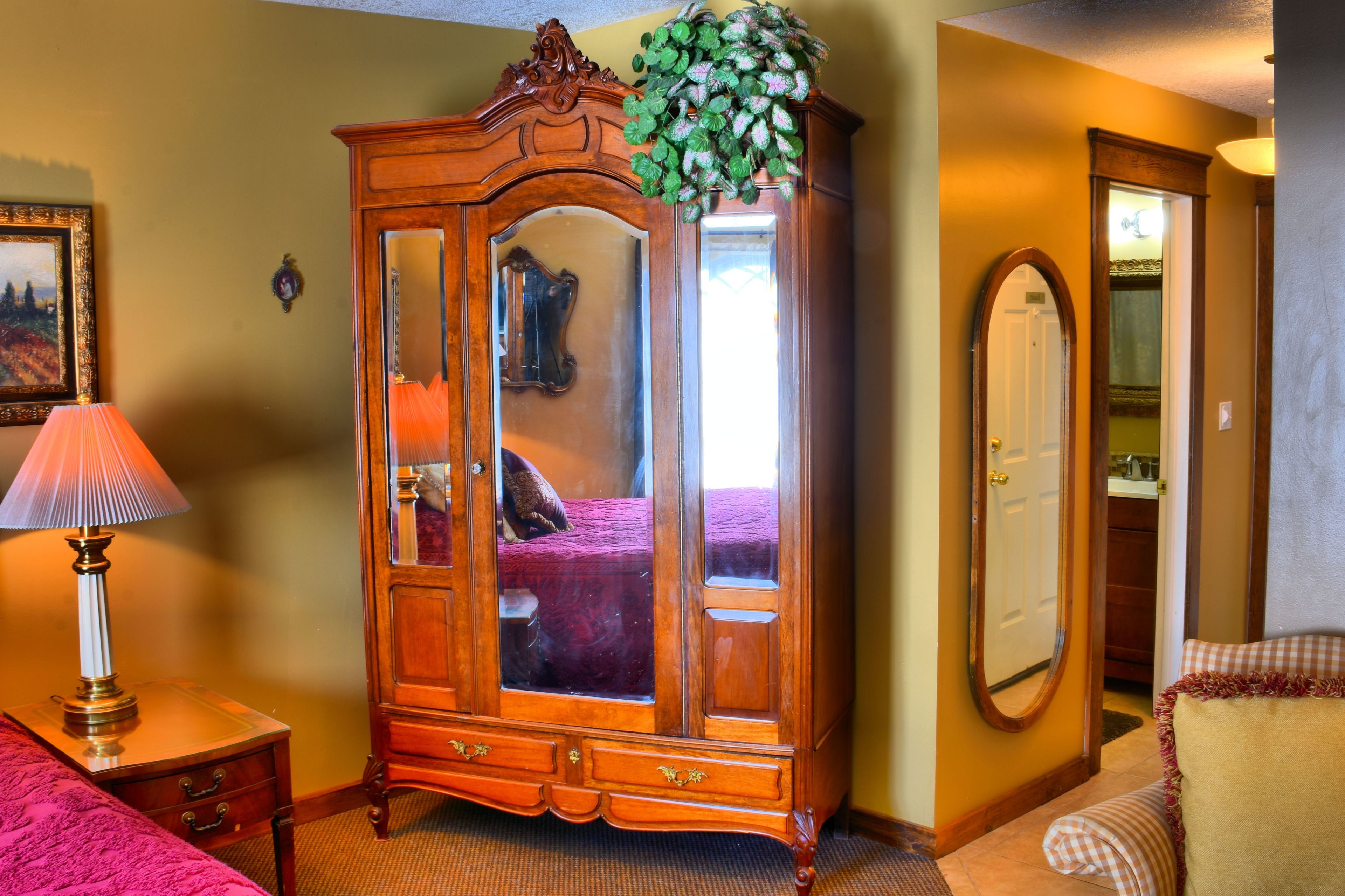 Una habitación con un armario de madera, una lámpara, un espejo y una silla a cuadros.
