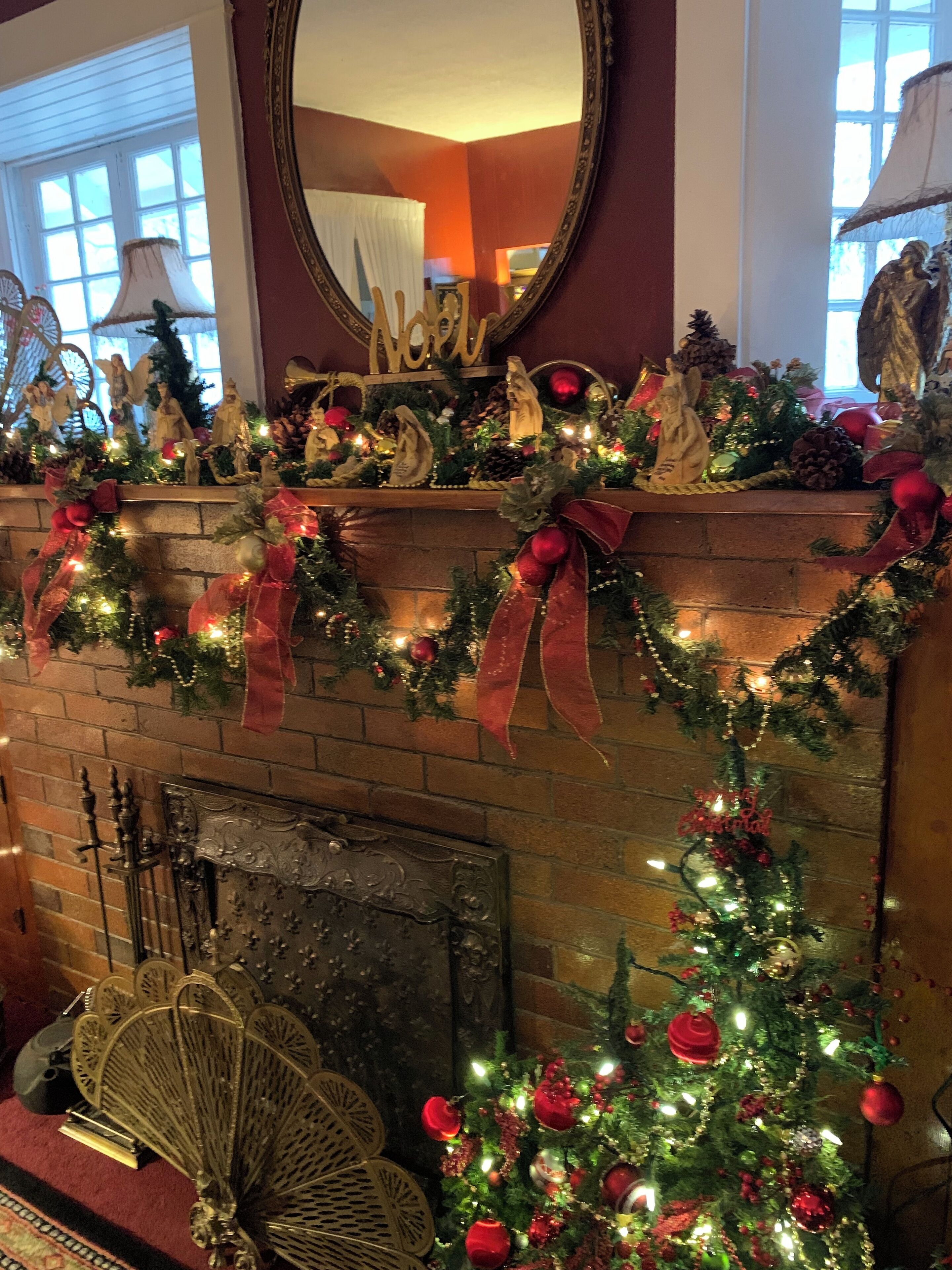Una chimenea con un árbol de Navidad, rodeada de adornos festivos y un espejo en la parte superior.