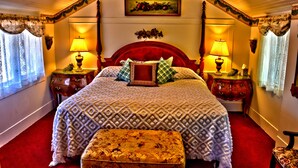 A traditional bedroom with a large bed, two bedside tables with lamps, a wooden bench, and a decorative wall hanging. - Bard's Inn (Cedar City)