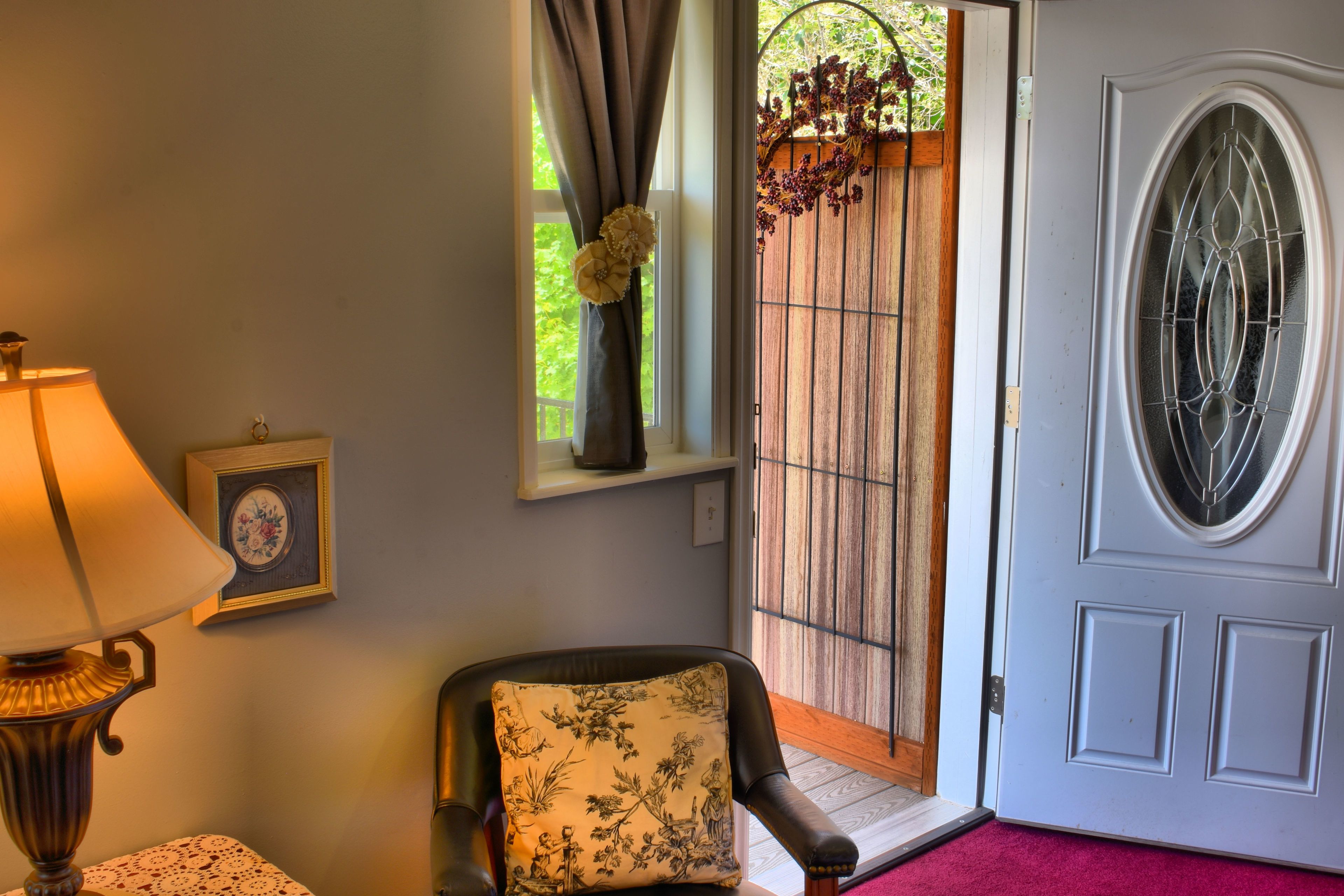 A room with a lamp, a chair with a floral cushion, a framed picture, and a door with a glass panel.