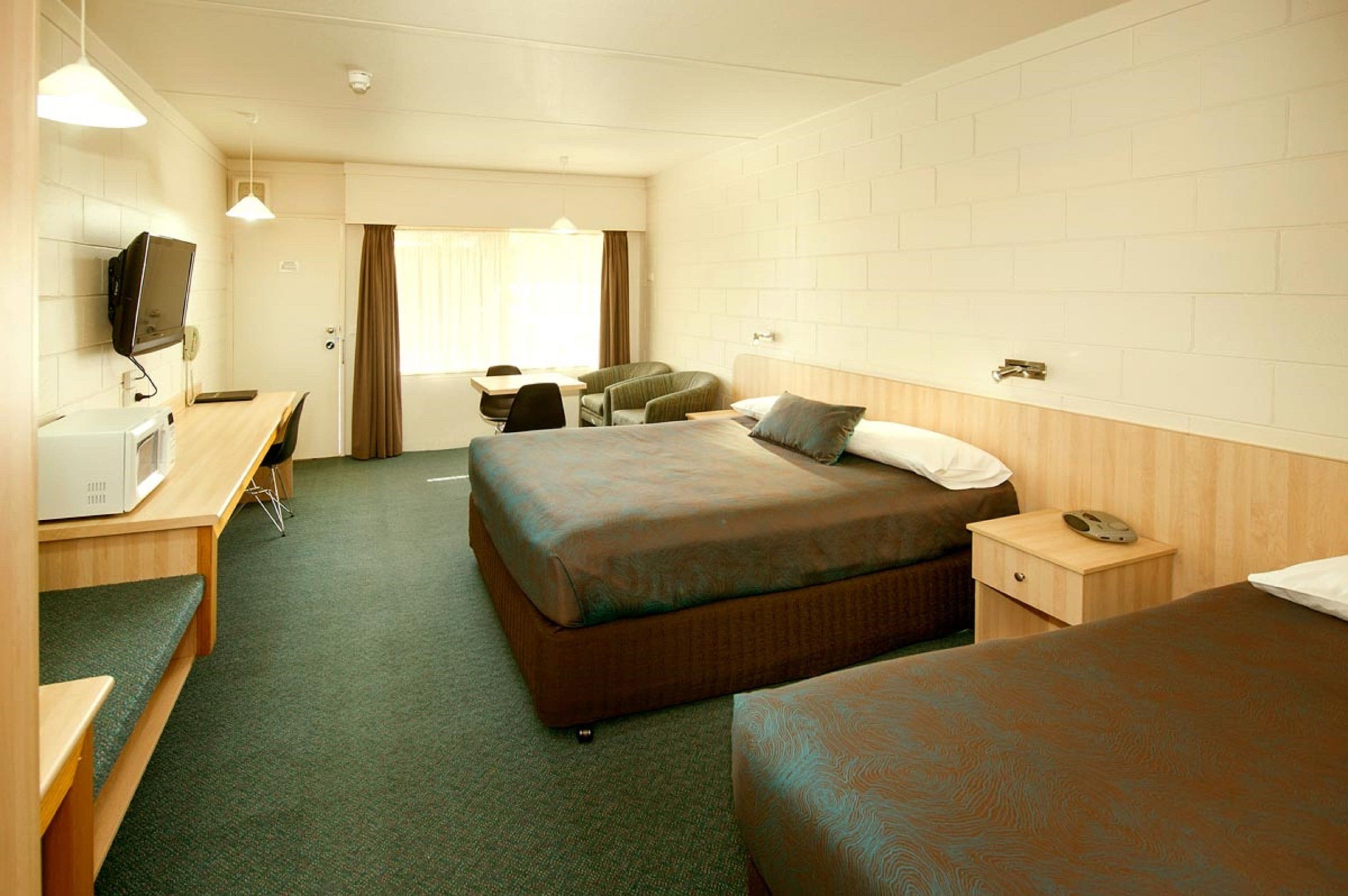 A hotel room with two beds, a desk with a computer, a television, and a window with curtains.