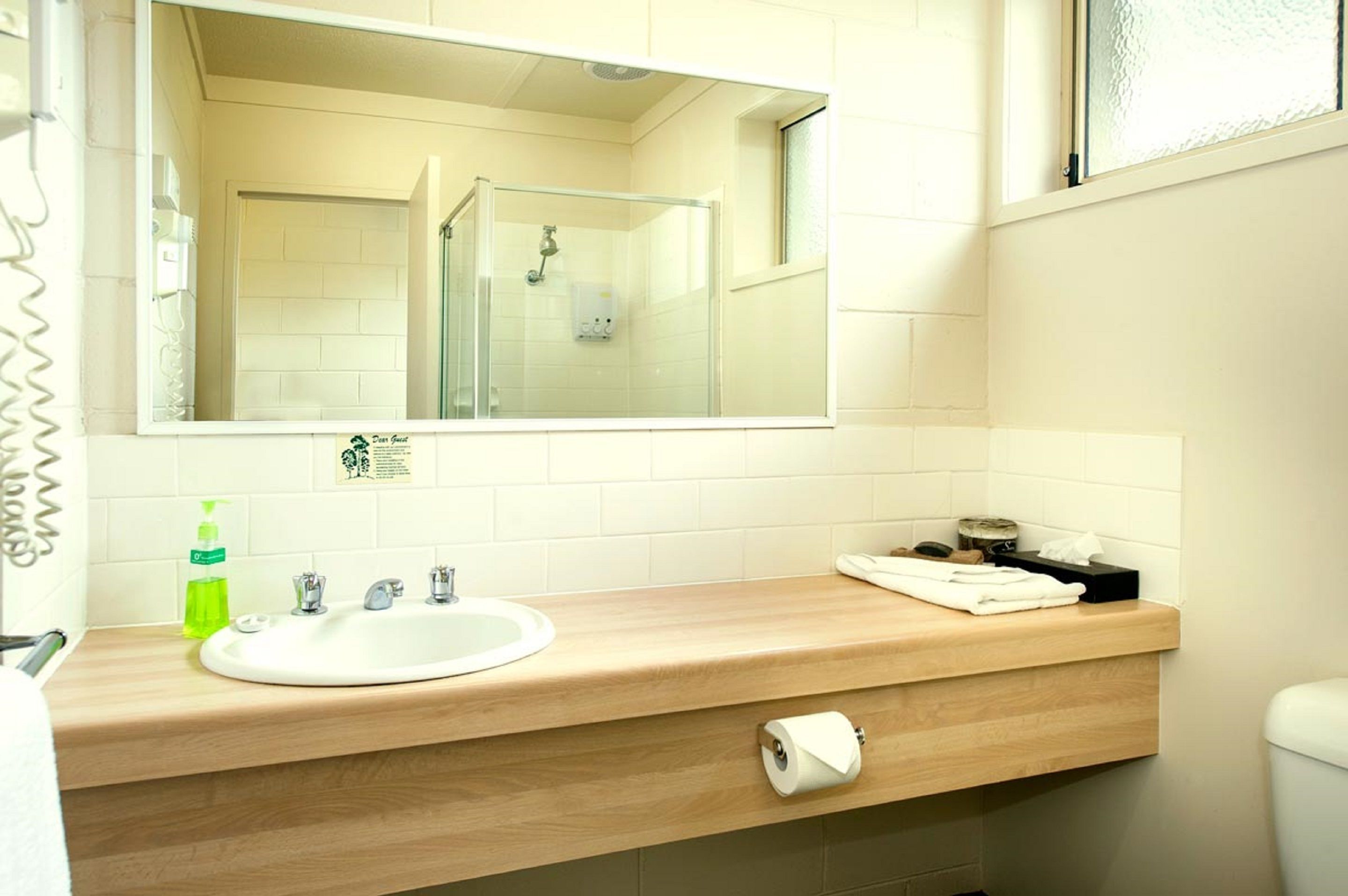 Ein Badezimmer mit weißem Waschbecken, einem Spiegel, einer Duschkabine aus Glas und einem Handtuchhalter.