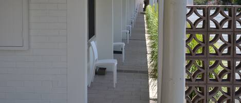 A covered walkway with white columns and benches, leading to a gate with a lattice design.