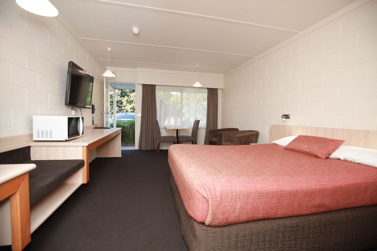 A hotel room with a bed, a desk with a microwave, a TV, and a view of the outdoors.