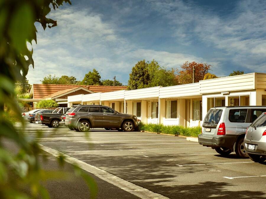 Un estacionamiento con varios coches aparcados frente a un edificio de techo plano y grandes ventanales.