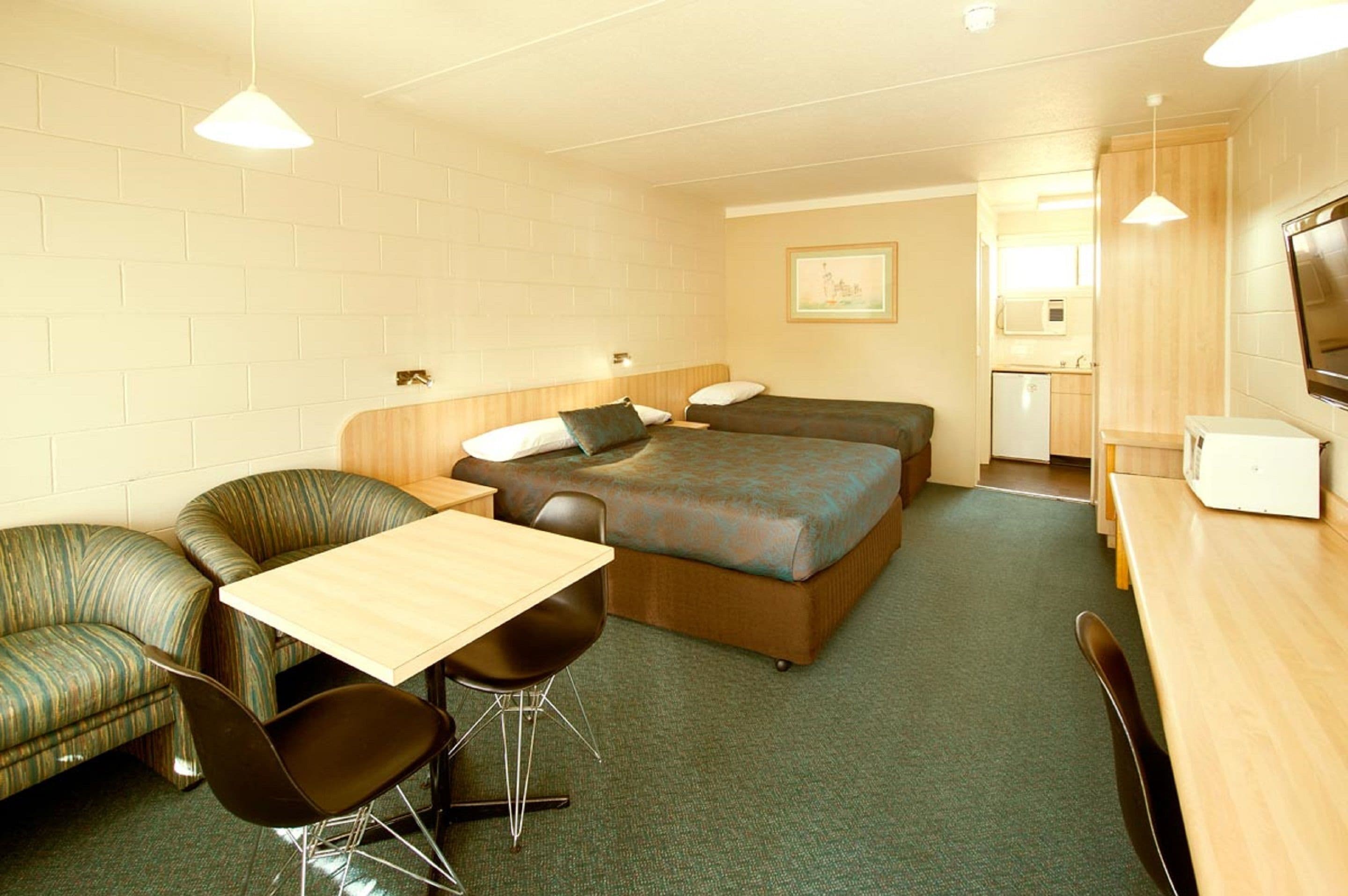 A compact hotel room with a single bed, a small kitchenette, a dining area with a table and chairs, and a sofa.