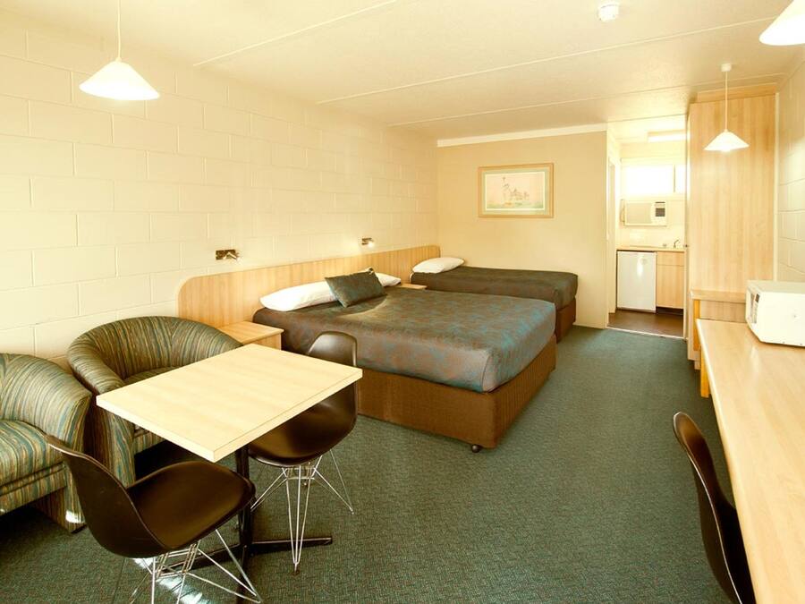 Habitación de hotel compacta con una cama individual, un pequeño rincón de cocina, una zona de comedor con mesa y sillas, y un sofá.