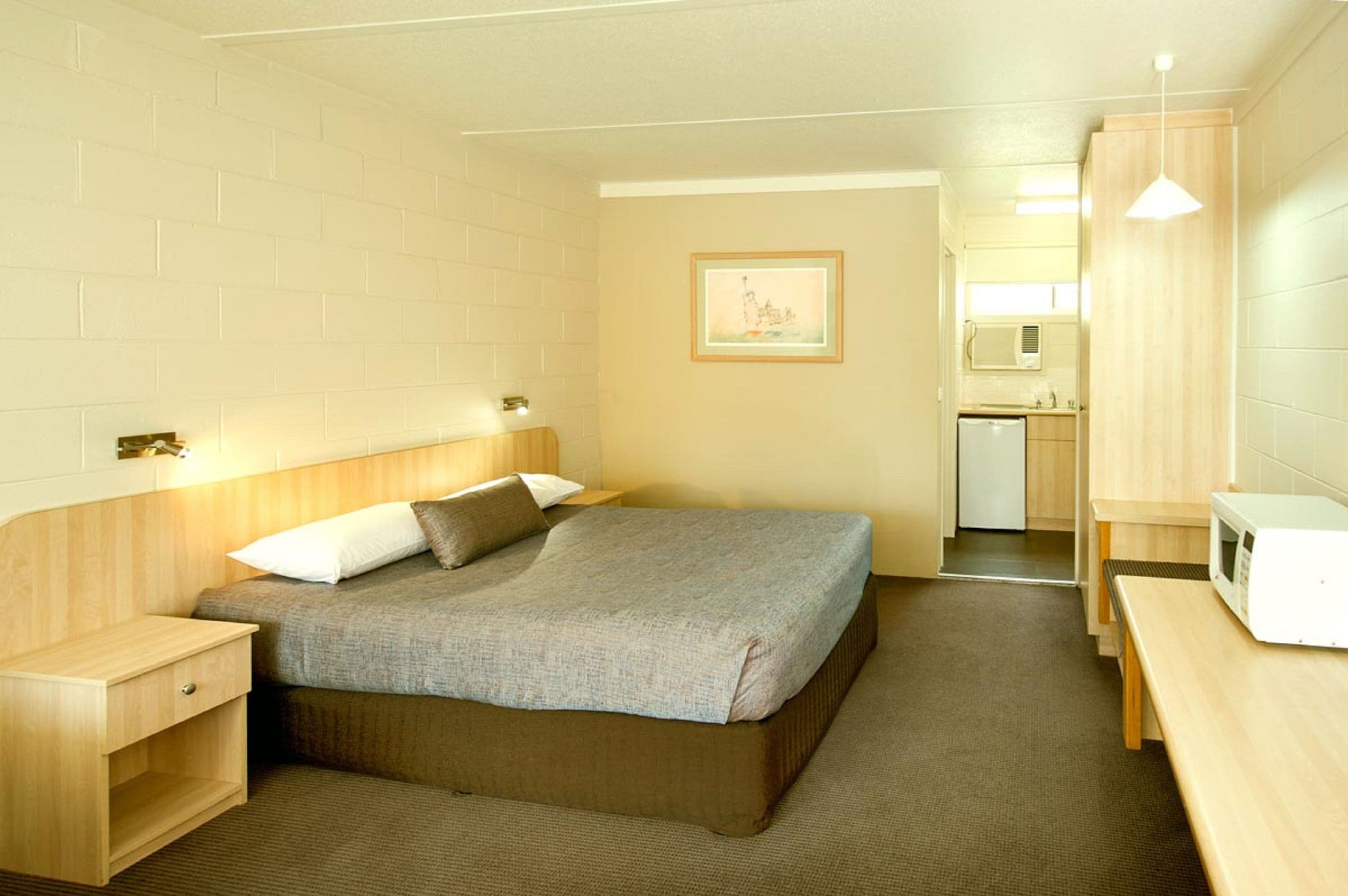 Una habitación de hotel compacta con una cama individual, mesita de noche y una pequeña zona de kitchenette.