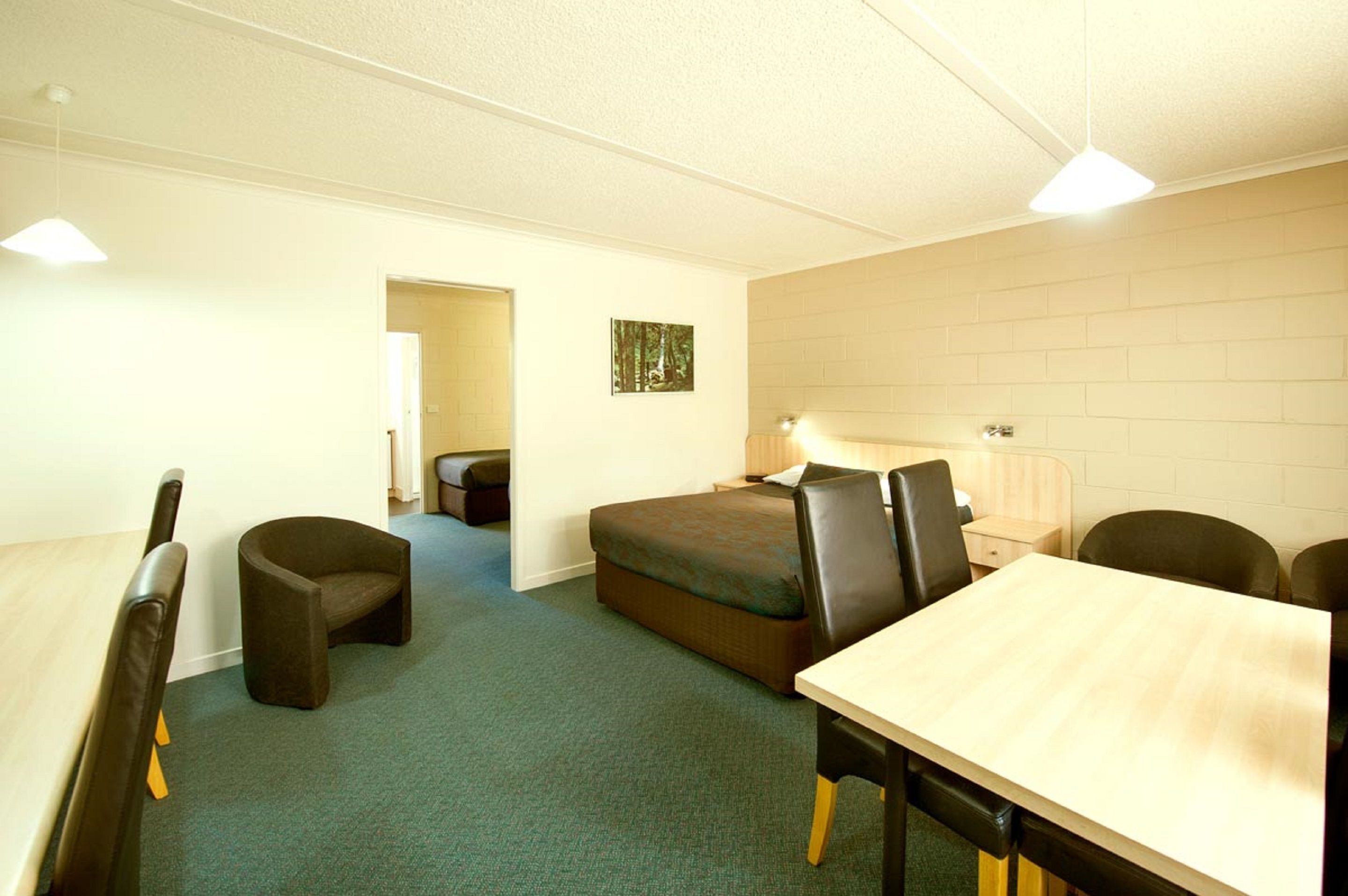 A room with a bed, a desk, two chairs, a small table, and a wall-mounted lamp.