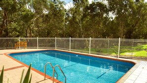 Uma piscina retangular com escada de metal e cerca branca ao redor.
