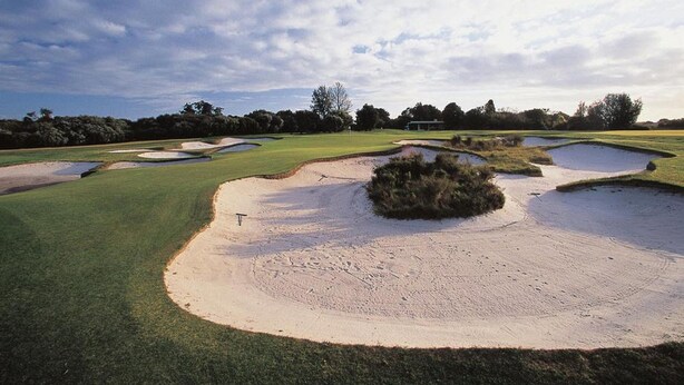 Um campo de golfe com bunkers de areia, putting green e um clube em segundo plano.