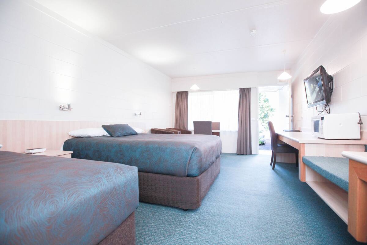A hotel room with two beds, a desk, a television, and a window with curtains.
