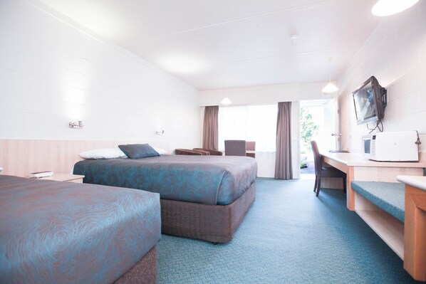 A hotel room with two beds, a desk, a television, and a window with curtains.