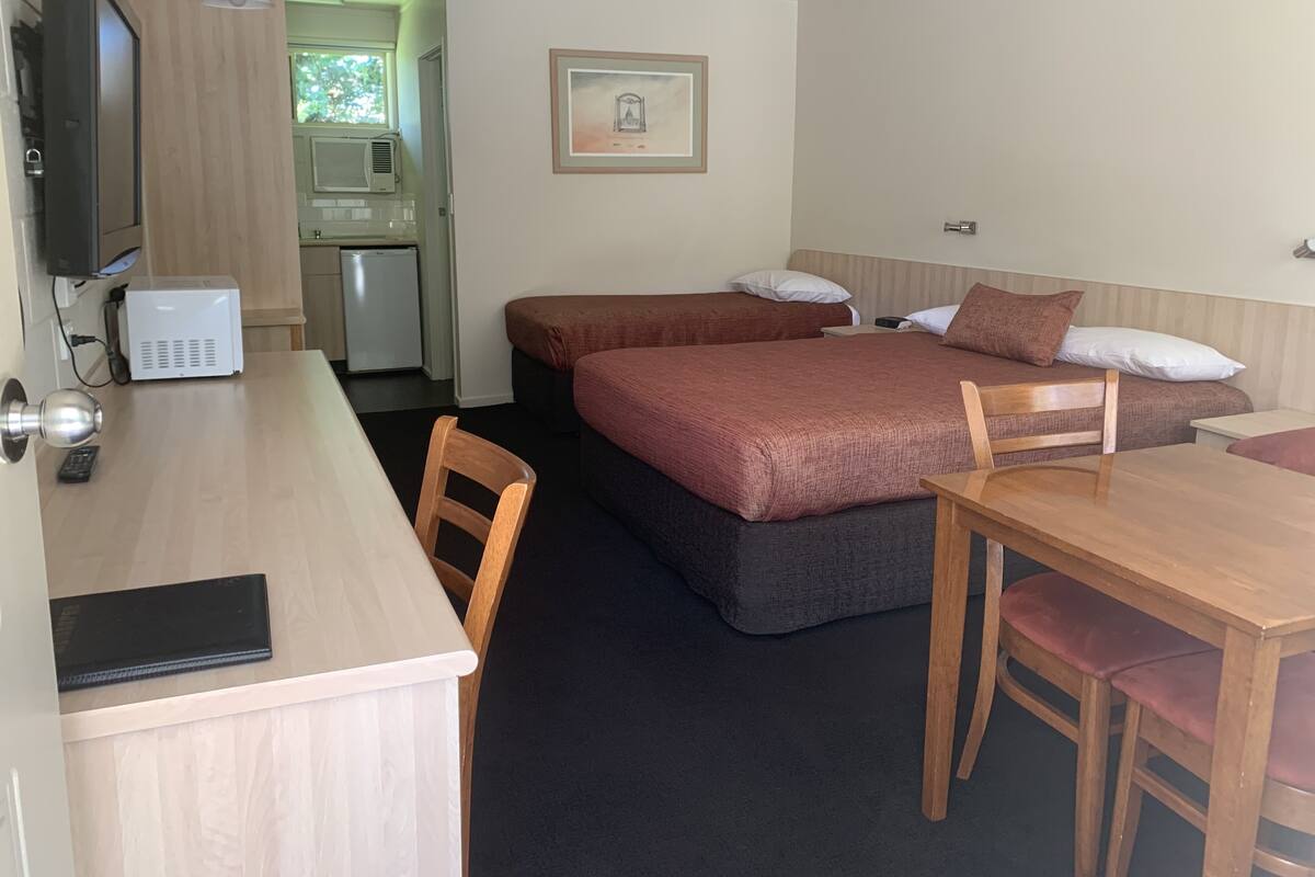 A compact hotel room with a bed, a desk, a chair, a microwave, and a television.