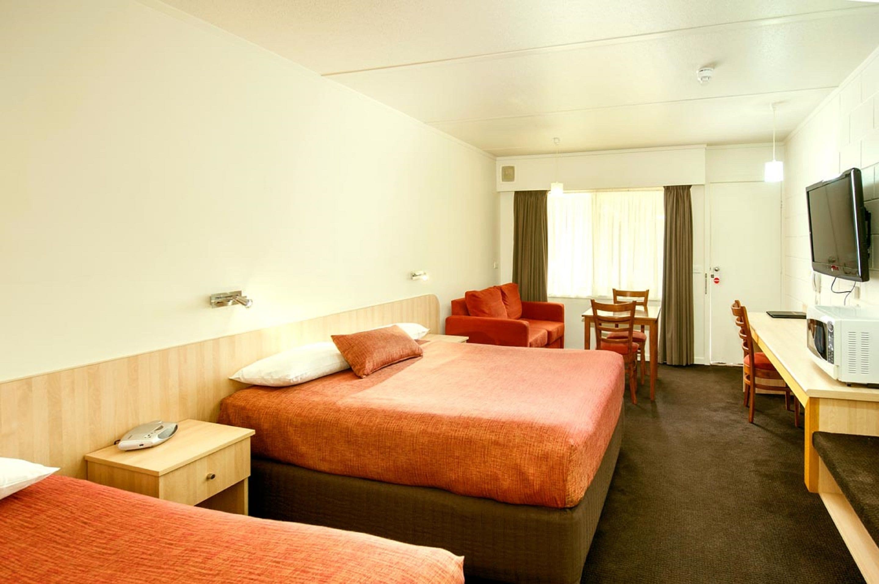 Habitación de hotel con dos camas, un escritorio con televisor y una silla.