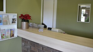 Um balcão de recepção de hotel com bancada de tijolos, uma planta em vaso e uma placa com o nome 'Box Hill Motel'.