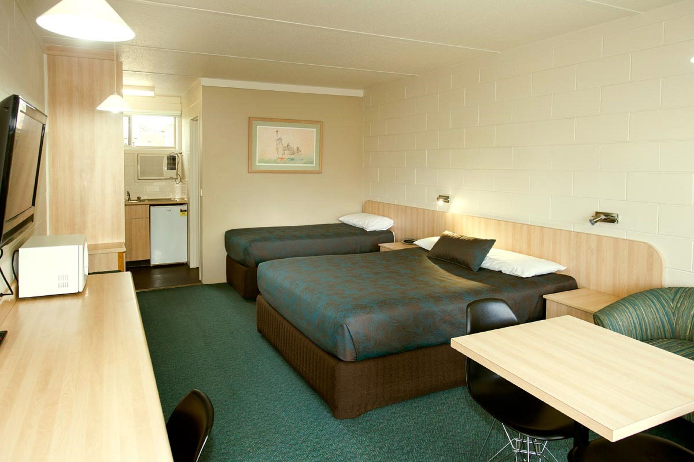 A hotel room with two beds, a desk, a chair, a microwave, and a small kitchenette.