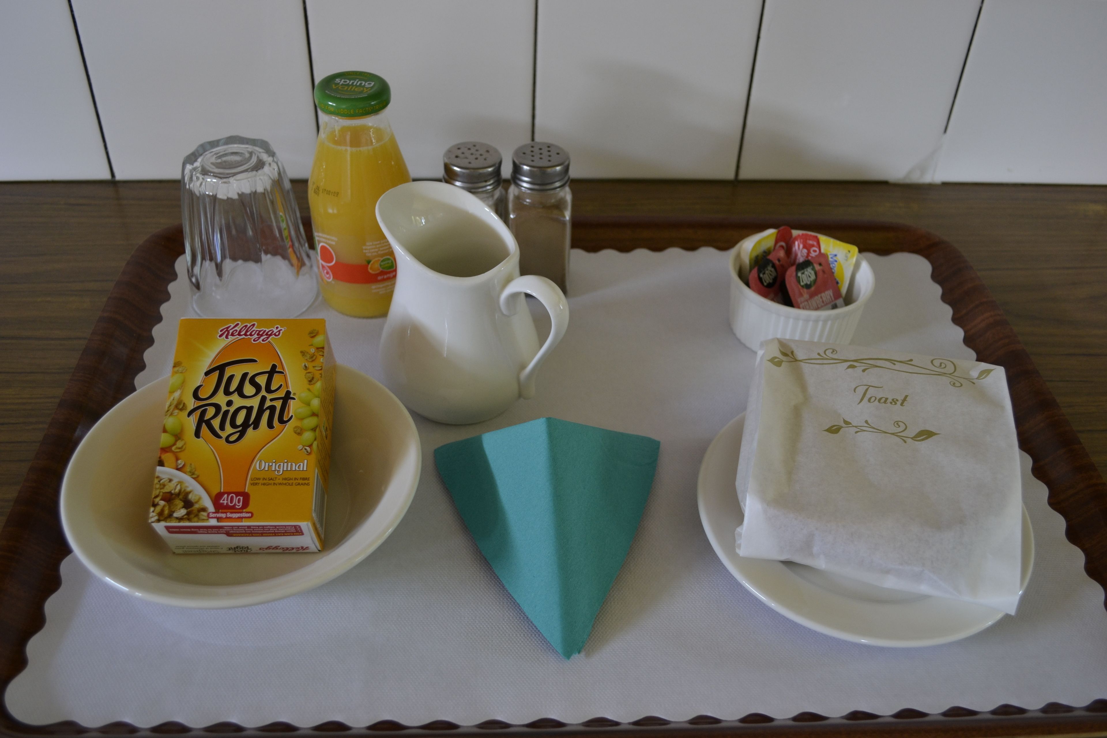 A tray with a box of Kellogg's Just Right cereal, a glass pitcher, a bottle of orange juice, salt and pepper shakers, a paper napkin, and a small bowl of strawberries.