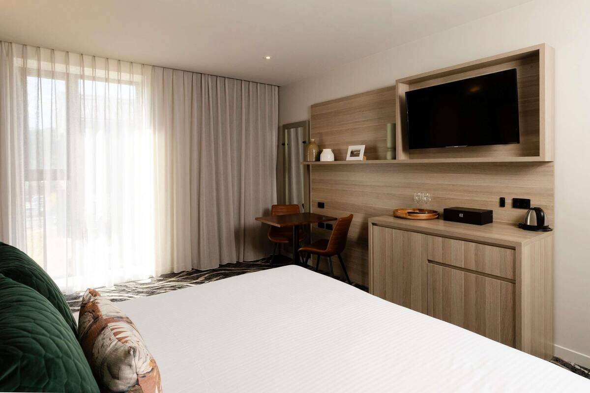 Una habitación de hotel con cama, escritorio, silla, televisor y cafetera.