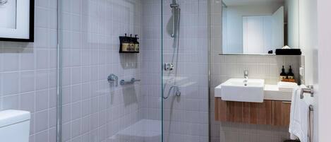 Un baño moderno con ducha de vidrio, lavabo blanco y tocador de madera.