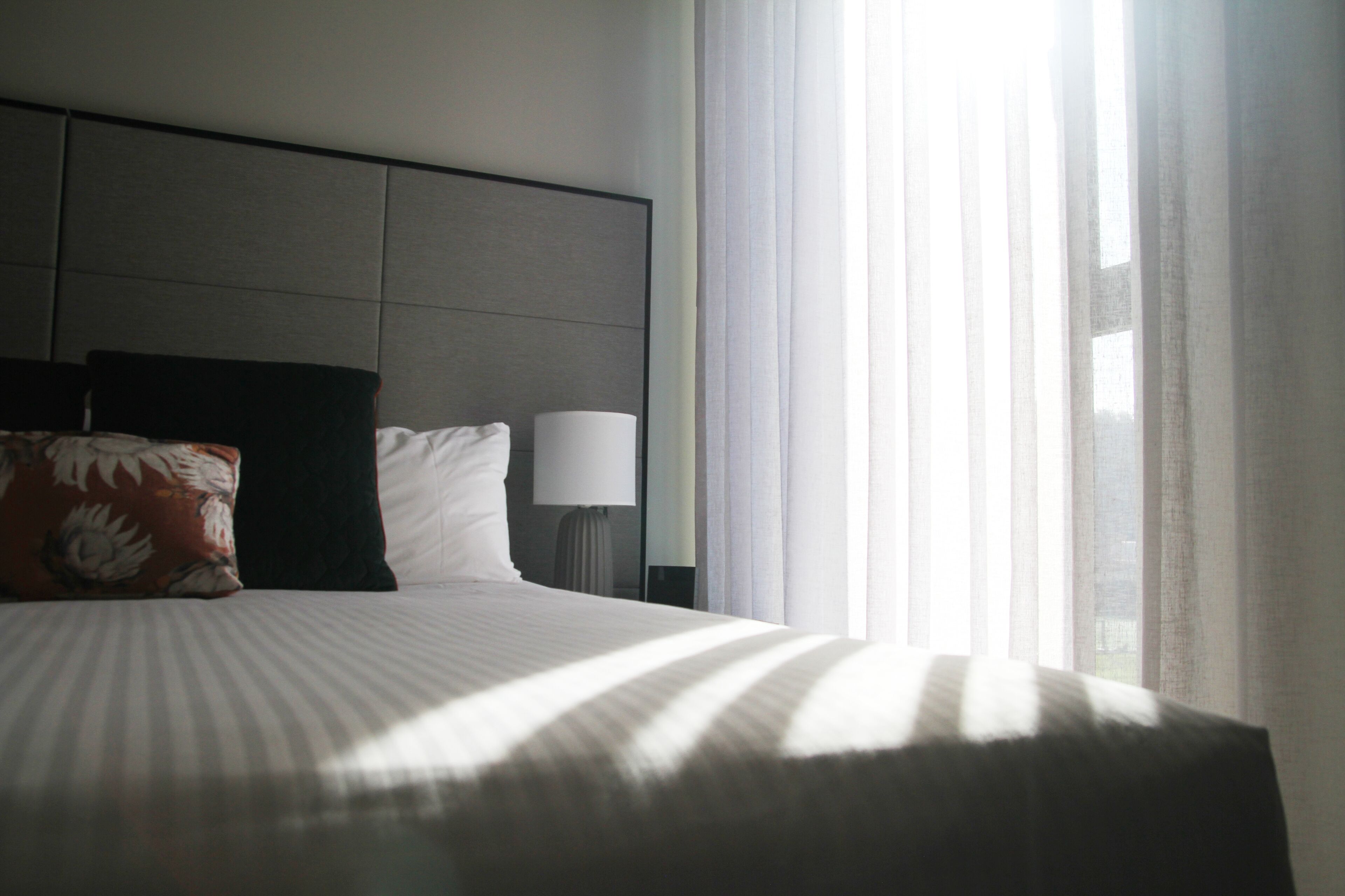 Een hotelkamer met een bed, kussens, een lamp en een raam met gordijnen.