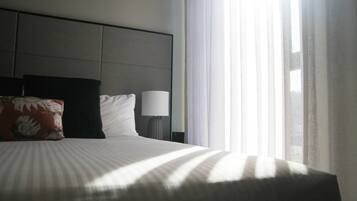 Een hotelkamer met een bed, kussens, een lamp en een raam met gordijnen.
