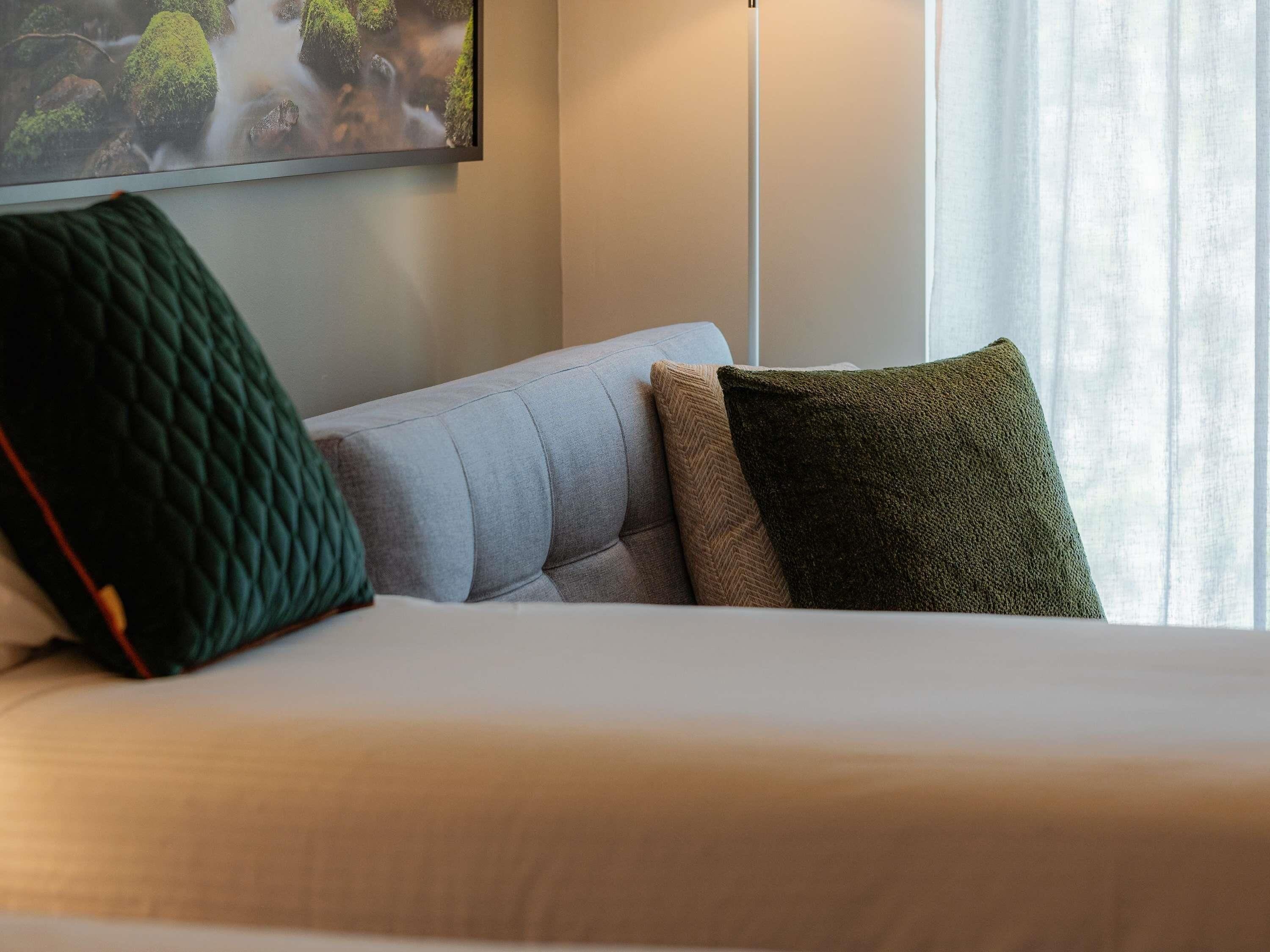 A bed with a white sheet, a grey sofa, and two pillows with different textures.