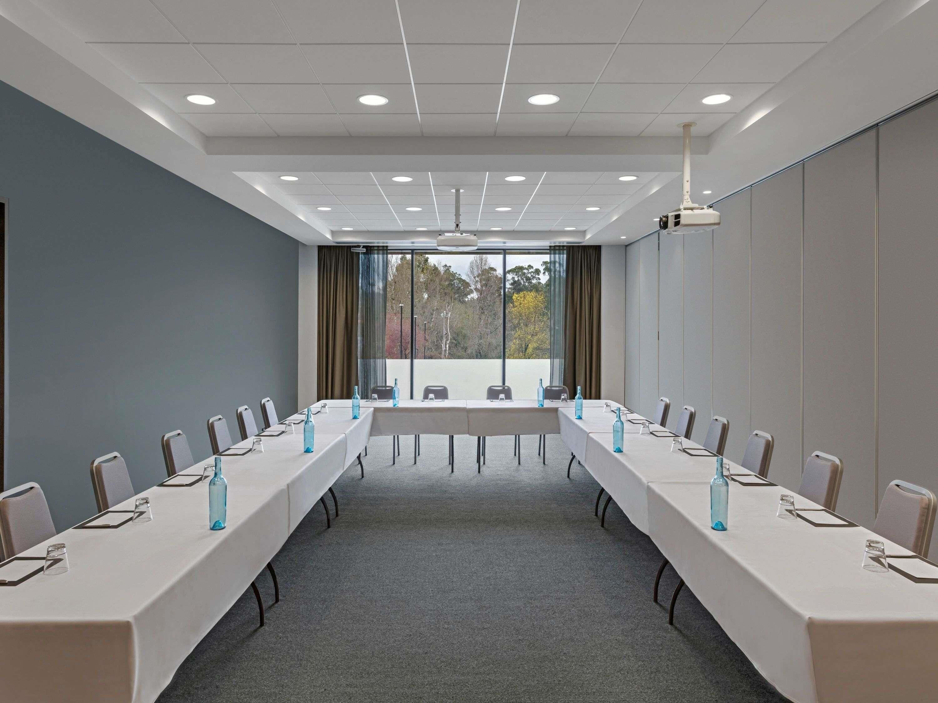 Ein Konferenzraum mit langen Tischen, Stühlen und einem großen Fenster mit Blick auf Bäume.