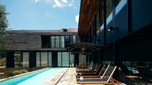 A modern pool area with lounge chairs and umbrellas, a stone-tiled pool, and a building with large windows and a wooden roof. - Peppers Marysville (Marysville)