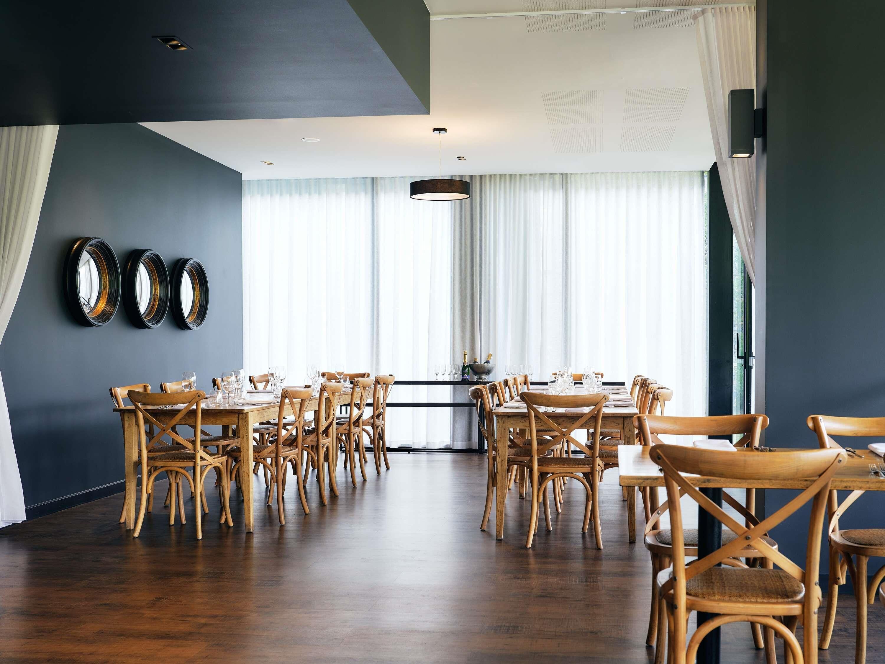 Comedor con sillas y mesas de madera, ventanas amplias con cortinas y espejos en la pared.
