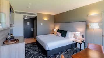 A hotel room with a bed, bedside tables, a desk, a chair, and a carpeted floor.