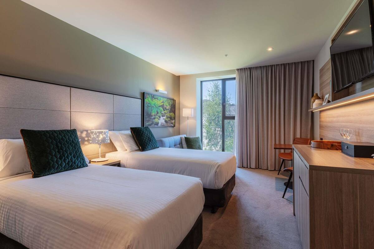 Una habitación de hotel con dos camas, un escritorio, un televisor y una ventana con cortinas.