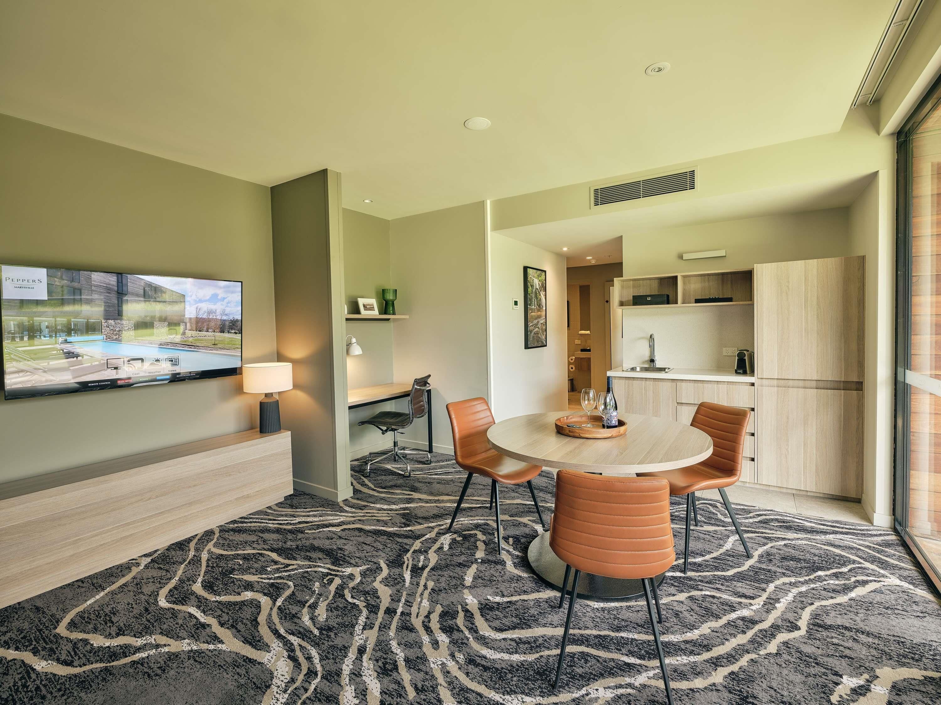 Una habitación de hotel moderna con comedor, televisor, cocina y un ventanal grande.