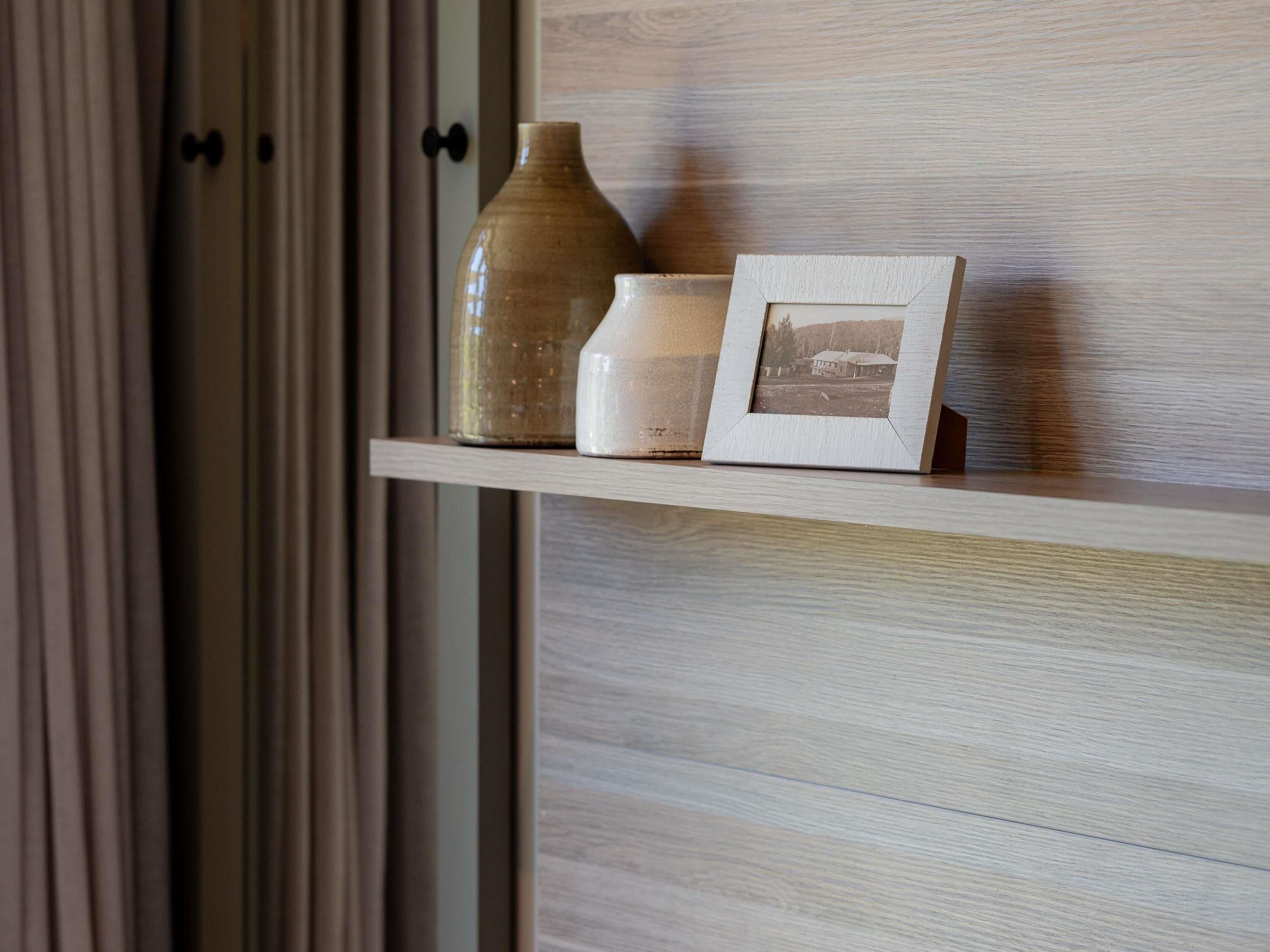 Une étagère avec un vase en céramique, un petit récipient blanc et une photographie encadrée.