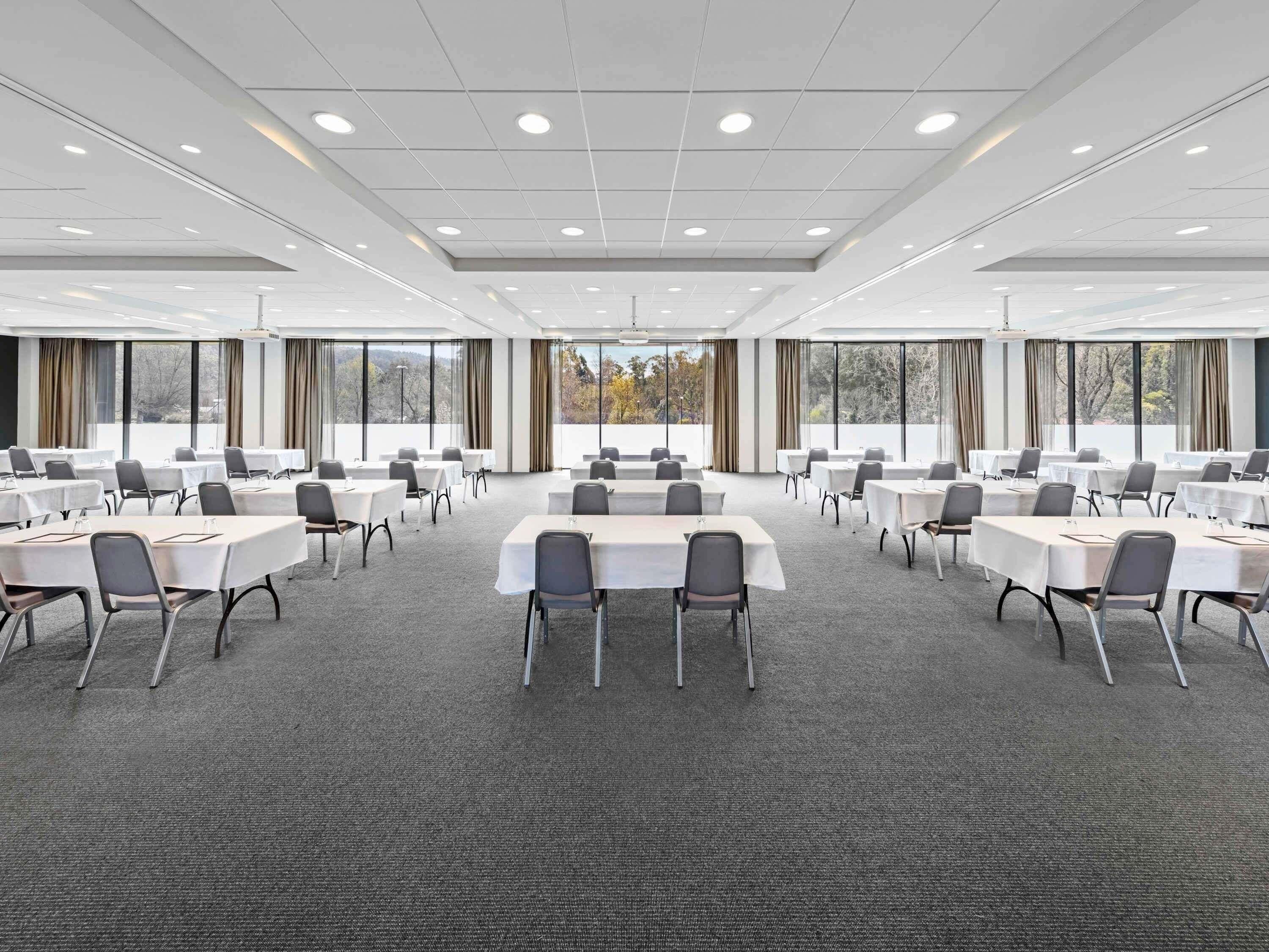 Un salón de conferencias con varias mesas y sillas, ventanas amplias y suelo alfombrado.