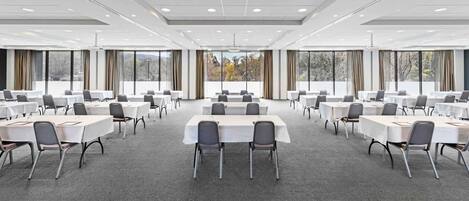 Un salón de conferencias con varias mesas y sillas, ventanas amplias y suelo alfombrado.