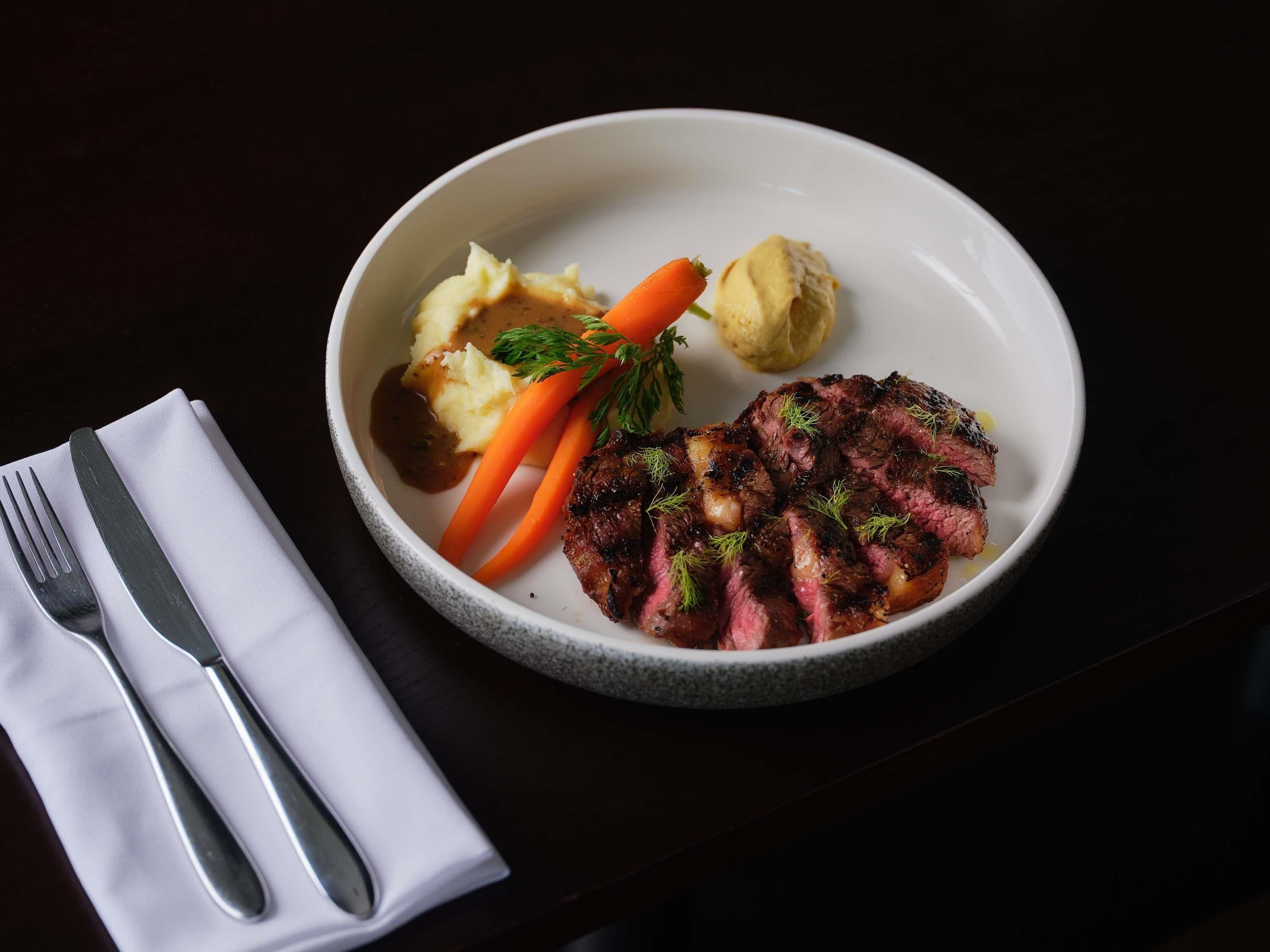 Prato com bife, purê de batatas, cenouras e molho.