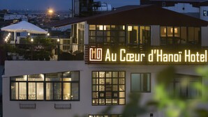 Exterior del Hotel Au Ceur d'Hanoi con señalización iluminada, amplias ventanas y una terraza en la azotea.