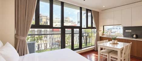 Una habitación de hotel con una cama grande, una mesa de comedor con sillas, una zona de cocina y un balcón con vistas a la ciudad.