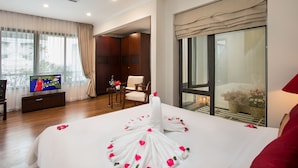 Una habitación de hotel con una cama grande, televisión, zona de estar con sillas y un balcón con vistas.