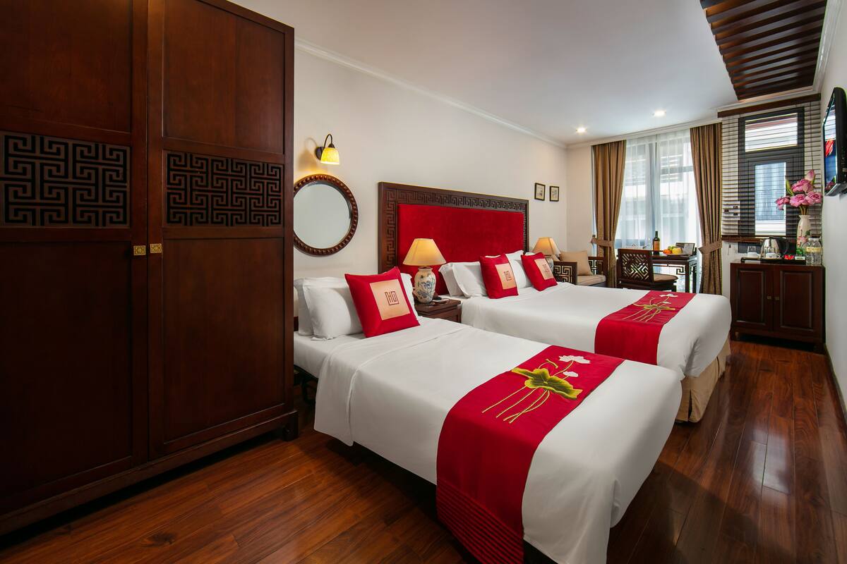 A hotel room with two beds, a large mirror, a wooden wardrobe, and a dining area with a table and chairs.