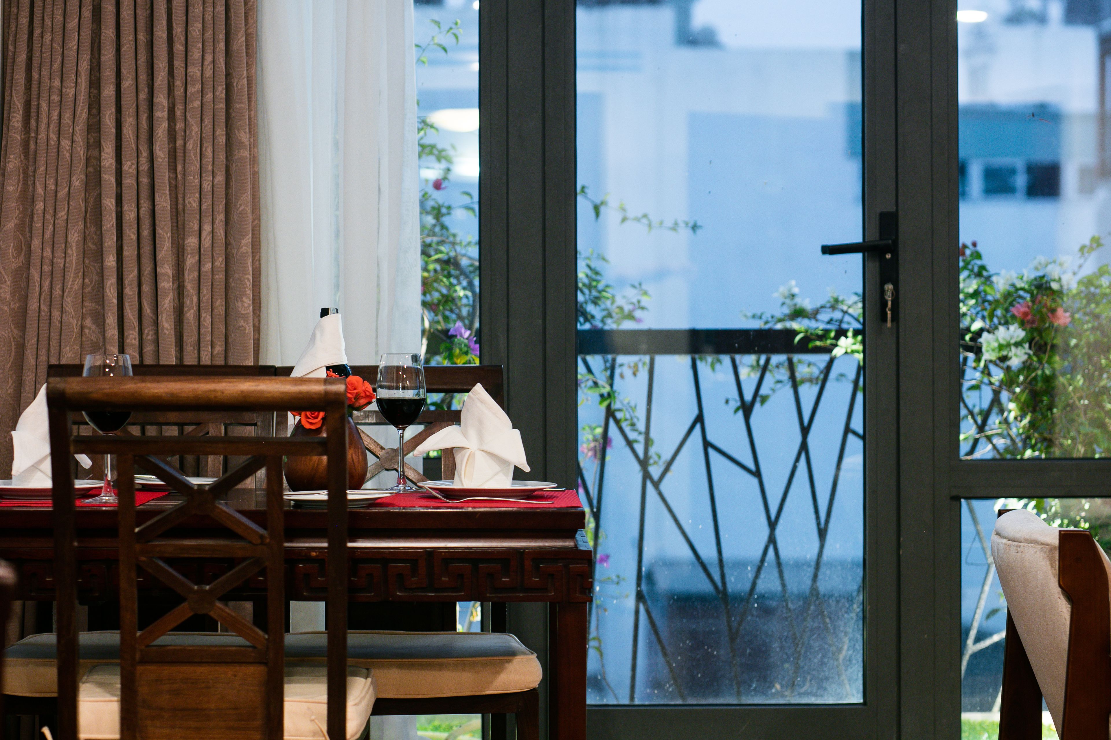 A dining area with a table set for two, a chair, and a view of the outdoors through a glass door.