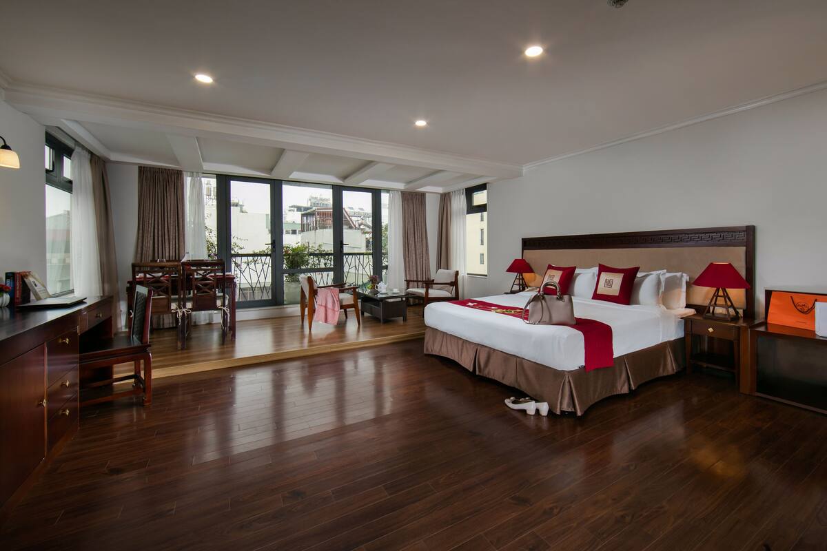A spacious bedroom with a large bed, a desk, and a balcony with a view.