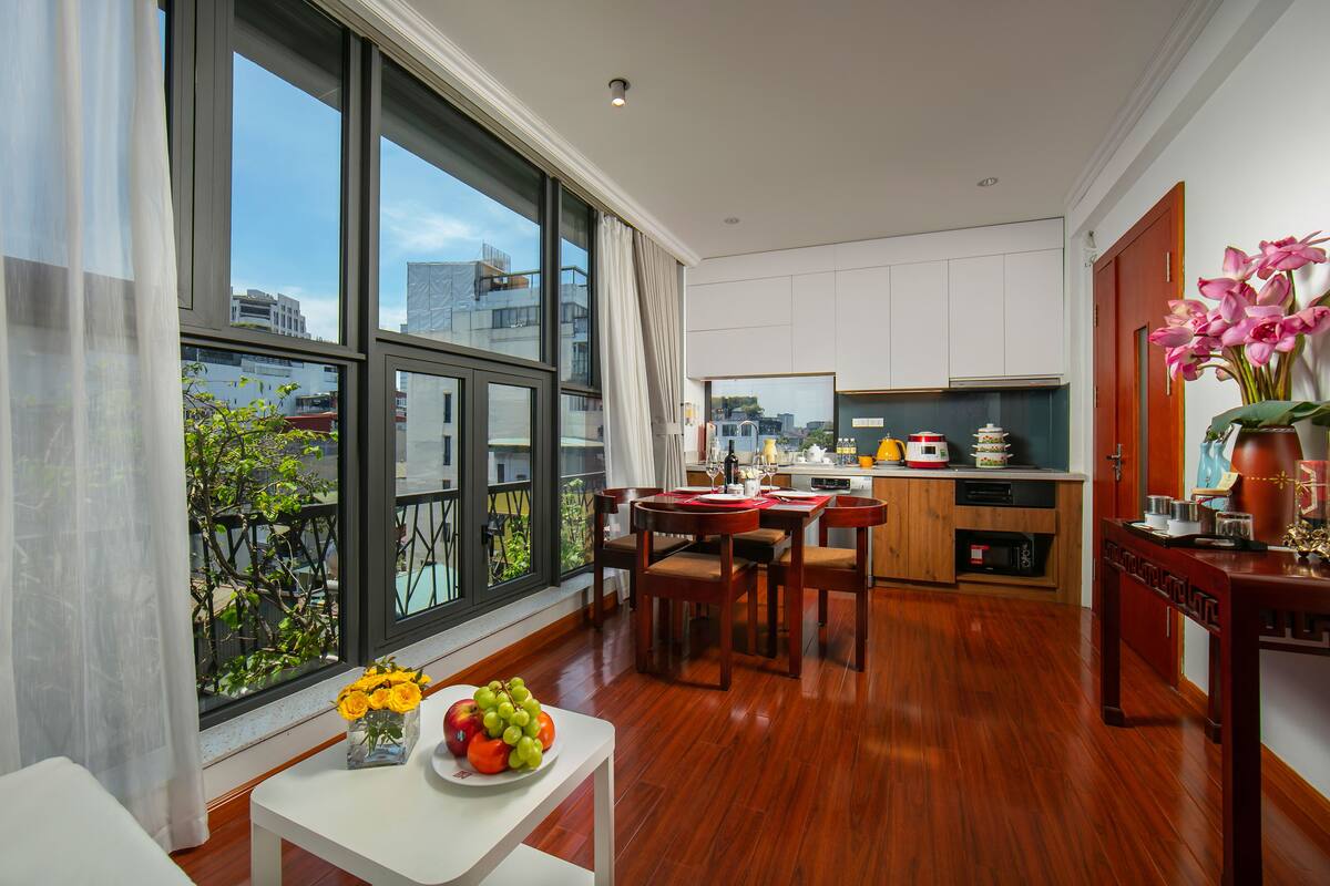 A modern kitchen with wooden cabinets, a dining area with a table and chairs, and a large window with a view of the city.