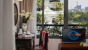 Una habitación con vista a un paisaje urbano, un jarrón con flores, un libro titulado 'VOGUE' y un televisor mostrando 'BREAKING NEWS'.