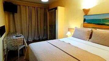 A hotel room with a bed, a desk with a chair, a TV, a painting on the wall, and a ceiling light.