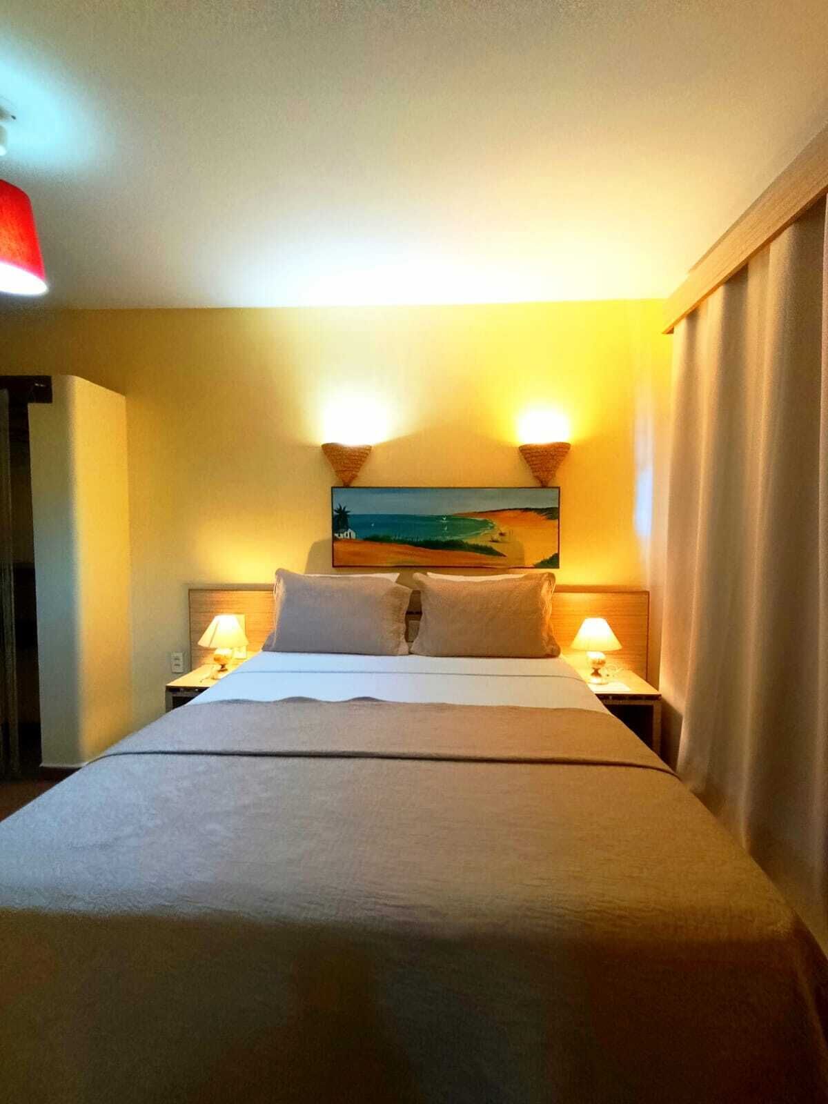 Un cuarto de hotel con una cama grande, dos lámparas de noche, un cuadro en la pared y vista al mar.