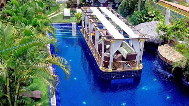 A floating platform with seating and a thatched roof, surrounded by a pool and palm trees. - Pousada Presidente Hotel (Aracati)