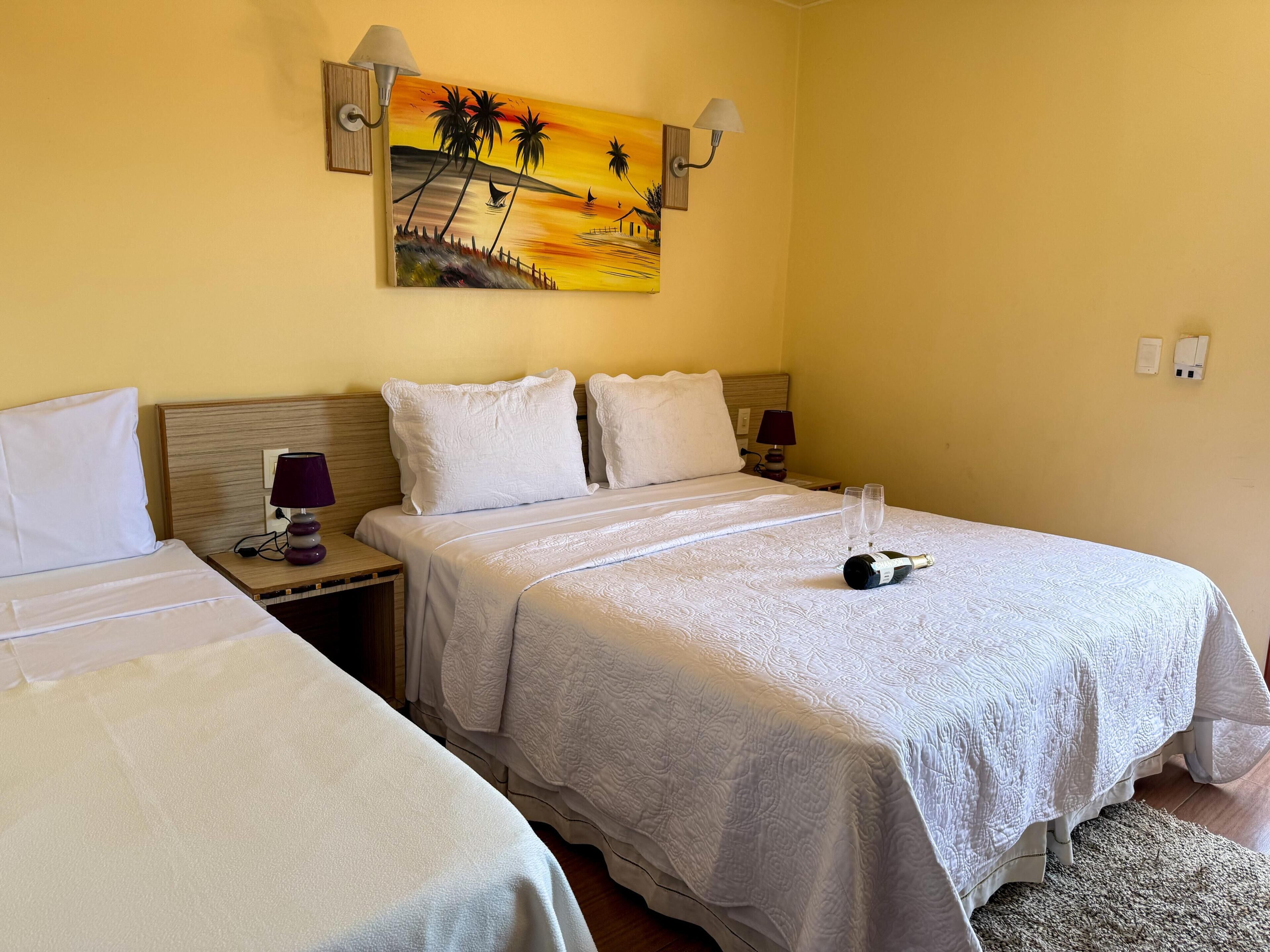 Habitación de hotel con dos camas, un cuadro de un atardecer y una botella de champán sobre la cama.